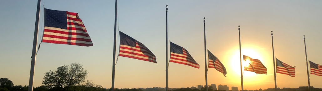 banner of american flags flying at half mast in front of a sunset