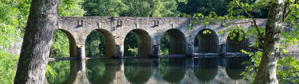 banner showcasing a stone bridge crossing a river in a wooded area